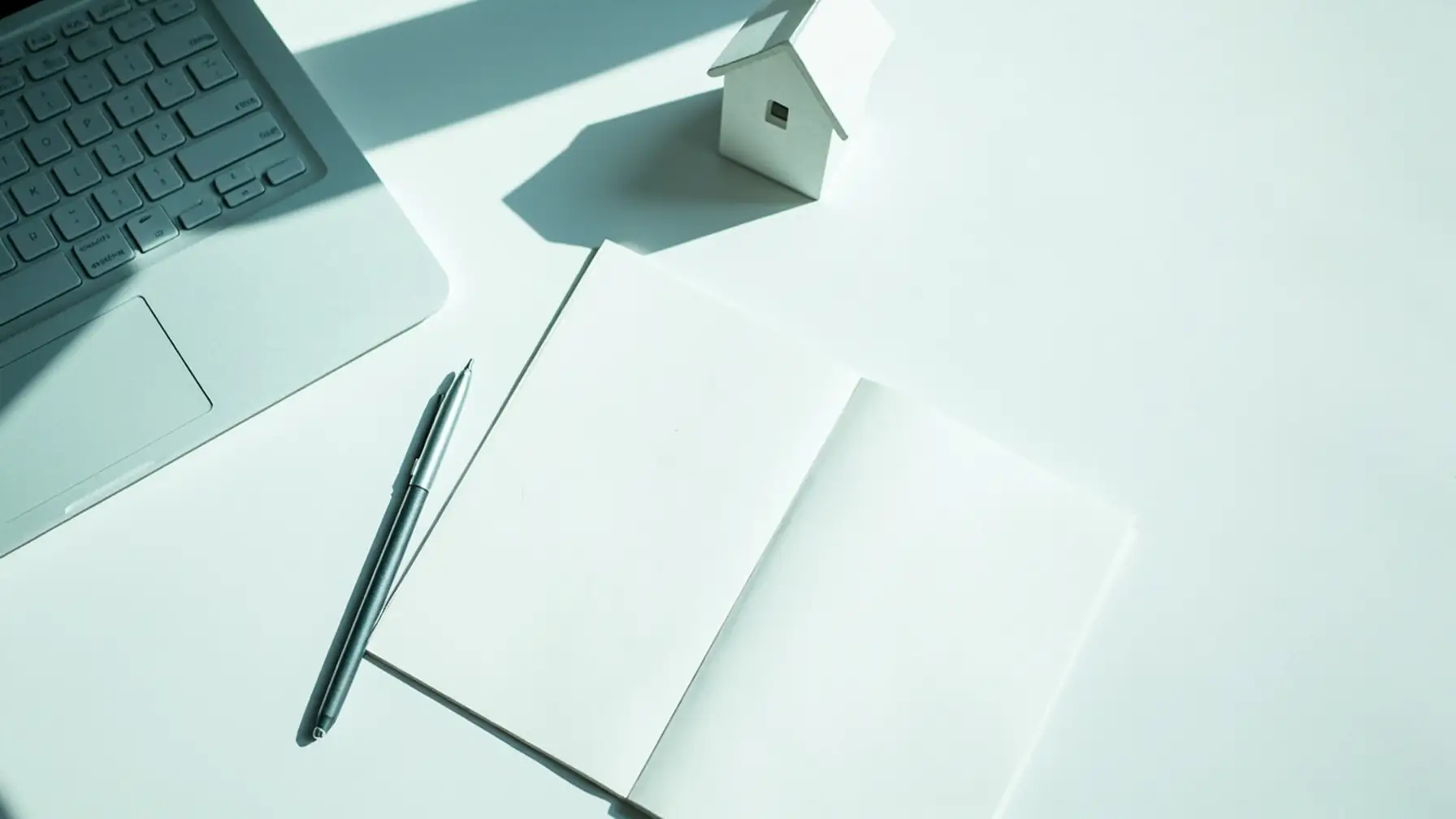Notebook e modelo de casa representando planejamento de consórcio imóvel para trabalho remoto